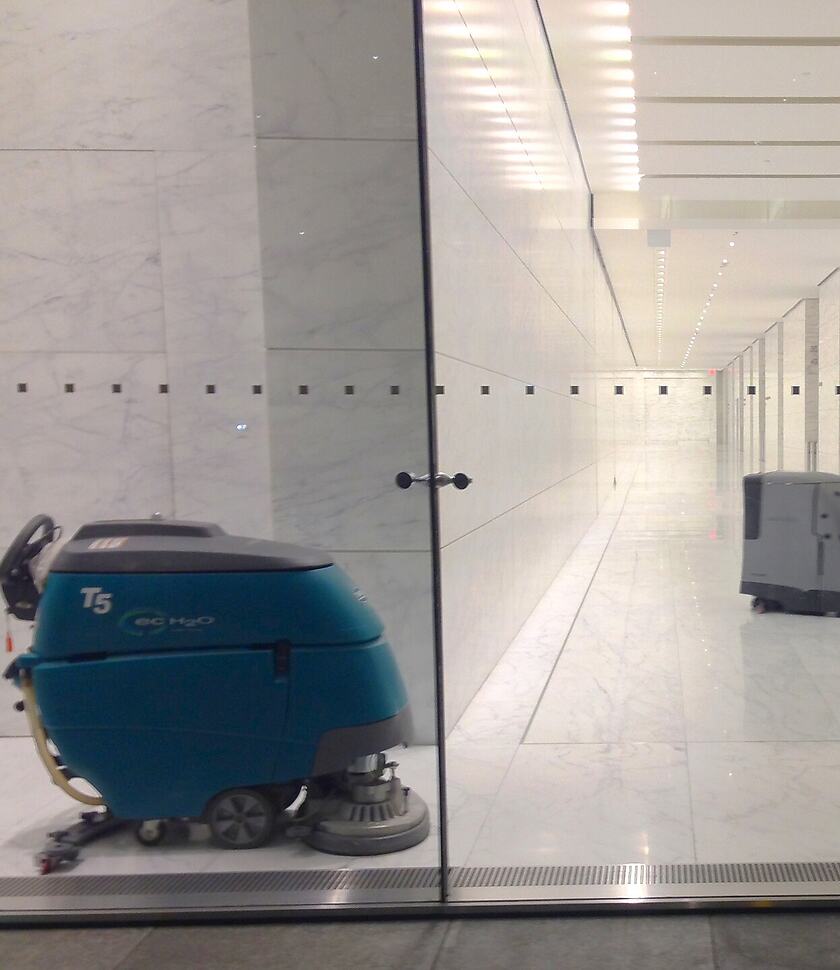 Professionele schrob-zuigmachine in een moderne kantoorhal met natuurstenen vloer